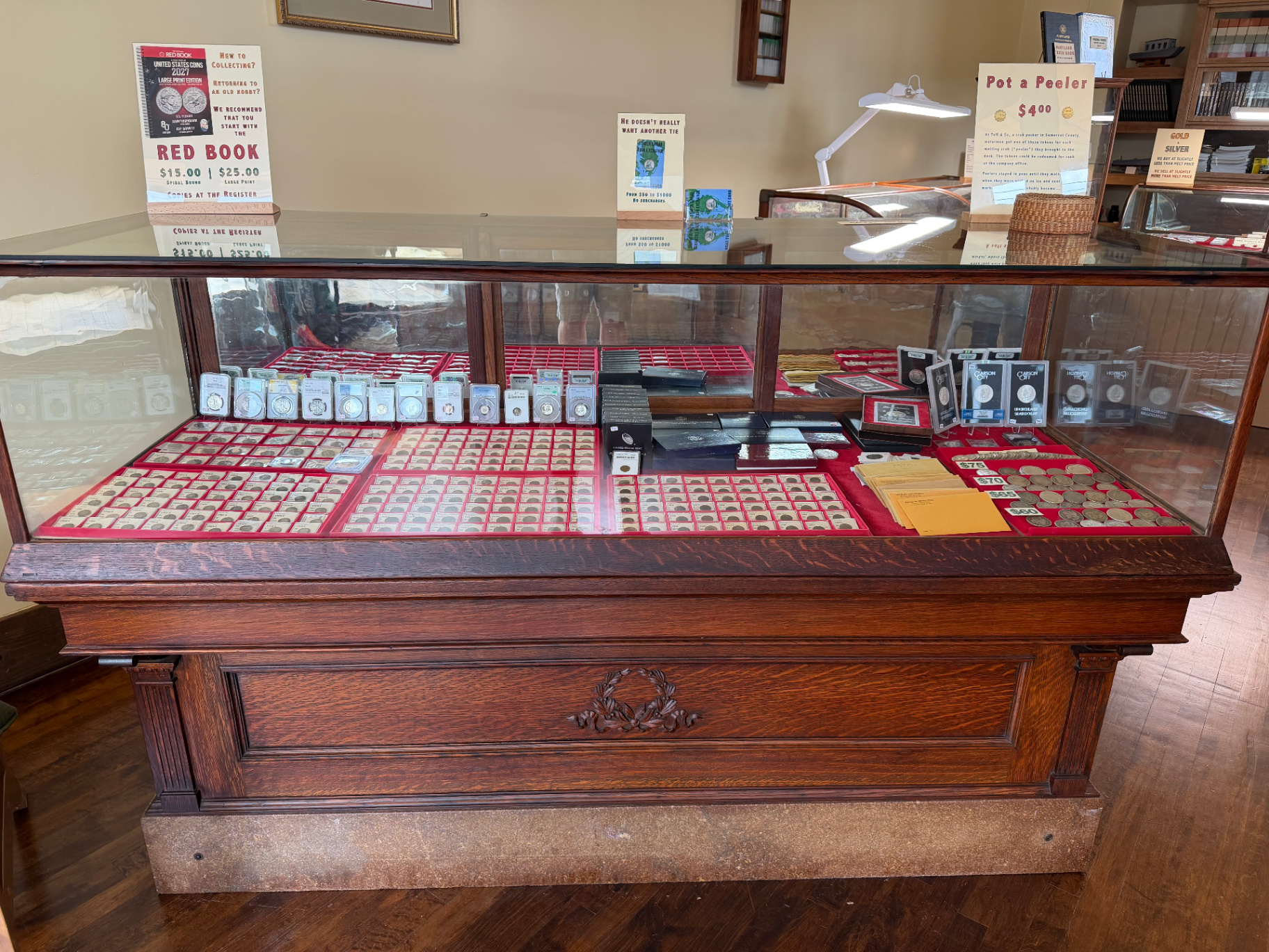 Close-up of an antique oak and glass display case filled with graded coins and Carson City silver dollars